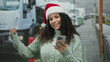 © Krakenimages.com - Woman outdoors wearing festive santa hat smiles holding phone on city street during winter.