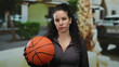 © Krakenimages.com - Woman holding basketball outdoors on sunny street with greenery in the background, showcasing a youthful athletic spirit and determination in casual wear.