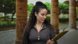 © Krakenimages.com - Woman wearing whistle holding clipboard in outdoor park setting with stone pillars and lush greenery providing a tranquil background for this scene.