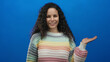 © Krakenimages.com - Woman in rainbow sweater gesturing with open hand against blue background showcasing expression and style.