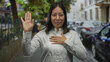 © Krakenimages.com - Woman standing with hand on chest on a city street near parked cars and iron fence, facing camera; gratitude reflection.