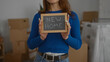 © Krakenimages.com - Woman holding new home sign in modern apartment surrounded by moving boxes showing excitement and fresh start in recently purchased indoor living space.