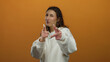 © Krakenimages.com - Woman points finger playfully against bright orange backdrop showcasing joyful expression and casual style in white sweater