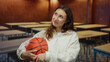 © Krakenimages.com - Woman holding basketball in classroom setting, young caucasian female smiling warmly, surrounded by empty desks, creating an educational and sporty atmosphere.