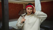 © Krakenimages.com - Woman holding racket indoors at construction site looking frustrated wearing sweatband in casual attire making hand gesture with brick wall background