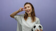 © Krakenimages.com - Woman smiling holding soccer ball making peace sign against isolated purple background shows youthful energy.