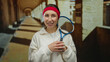 © Krakenimages.com - Woman holding a tennis racket indoors wearing a red headband at an old university corridor.