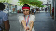 © Krakenimages.com - Young woman with medal posing playfully on city street, wearing red headband and white shirt, with finger gun gesture against urban backdrop.