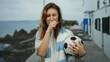 © Krakenimages.com - Woman holding soccer ball on beach promenade wearing scarf exhibiting emotions under cloudy sky.