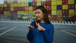 © Krakenimages.com - Woman in blue sweater gestures in port with containers stacked in background suggesting new opportunity or presentation outdoors.