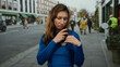 © Krakenimages.com - Young woman in blue sweater with vote badge touching hair on city street in the united states, expressing concern and curiosity outdoors among people walking.