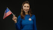© Krakenimages.com - Young woman holding usa flag and wearing vote badge against an isolated black background, symbolizing american civic engagement and patriotism.