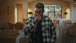 © Krakenimages.com - Man covers nose with hand in a restaurant dining area inside a building, plaid shirt, standing near set tables and window light; disgust avoidance.