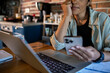 © Marko Geber - Woman using smartphone and laptop in home kitchen