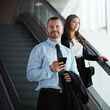 © peopleimages.com - Thinking, businessman and smile with smartphone, escalator or travel with flight schedule on website. Moving, stairs and person with mobile for commute, airport and reflection for international trip