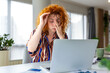 © Graphicroyalty - Tired redhead woman with glasses rubbing eyes while working on laptop at home office. Exhausted female professional suffering from eye strain and headache. Professional burnout concept.