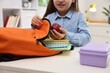 © New Africa - Girl with apple packing her backpack for school at desk indoors, closeup
