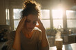 © EricMiguel - Young woman holding her temples in a sunlit kitchen beside a steaming mug of coffee, conveying morning exhaustion and quiet contemplation