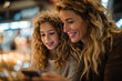 © EricMiguel - Smiling mother and daughter sharing a warm moment while looking at a smartphone together in a cozy indoor market with soft bokeh lights