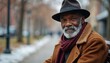 © Vadym - Elderly african american man wears hat scarf coat sits park bench. Mature person looks at camera with calm smile. Urban winter scene with soft snowy background and trees.