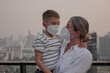 © blackday - Mother holding young child while both wear protective face masks on rooftop with city skyline