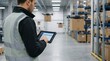 © MIKHAIL - Logistics worker in high visibility vest uses digital tablet to control autonomous drones and manage packages in a smart warehouse, demonstrating automated supply chain efficiency