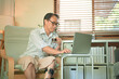 © Prathankarnpap - Middle-aged man working on a laptop at home while wearing a prosthetic leg, focused remote work