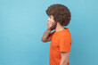 © khosrork - I won't tell. Portrait of man with Afro hairstyle wearing orange T-shirt covering mouth with hand, keeping secret, terrified with shocking news Indoor studio shot isolated on blue background.