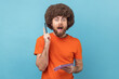 © khosrork - Portrait of excited man with Afro hairstyle wearing orange T-shirt writing creative idea into notebook, drawing sketch or taking notes in paper. Indoor studio shot isolated on blue background.