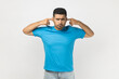 © khosrork - Portrait of annoyed sad unshaven man wearing blue T- shirt standing covering ears with fingers, does't want to hear unpleasant sounds. Indoor studio shot isolated on gray background.
