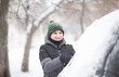 © zulfiska - A smiling child in a winter jacket and hat cleans snow off a car during a heavy snowfall, outdoor winter scene.