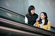 © Parichat - Two young Asian women riding escalator talking
