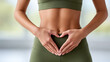 © Ally_art - Close up of woman's hands forming a heart shape on her stomach in green sportswear