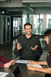 © Stock 4 You - Smiling young ceo leader businessman entrepreneur in glasses gestures while leading discussion with female colleagues or partners in modern office. Women take notes, collaborative atmosphere. Vertical