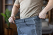 © Liubomir - Man demonstrating successful weight loss and health transformation, holding out the waist of his loose, oversized jeans, symbolizing achievement in diet and fitness
