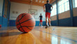 © Vadym - Basketball rests on polished wood gym floor, players run in blurred background. Active game, indoor sport, competition, athletic team training, focus on ball.