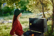 © SHOTPRIME STUDIO - Young woman in a green cap enjoying a summer barbecue outdoors, surrounded by trees and greenery, showcasing a joyful attitude and a sense of relaxation
