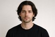 © Vladyslav Tykhonov - Studio portrait of a young man with medium-length wavy hair and subtle stubble wearing a black shirt against a neutral light background