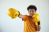 Young boy with afro hair wears yellow boxing gloves. He smiles while posing with his fists up. Kid looks energetic ready for sport or martial arts training session.