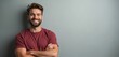 © Viktor - Bearded man with crossed arms smiles warmly. He wears a red tee shirt, standing casually against a plain grey wall. Friendly, approachable, confident pose.