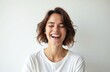 © Viktor - Young woman laughs heartily with eyes closed against white backdrop. She wears simple white t-shirt, her expression conveys pure joy and mirth. Her brown hair is styled casually around her shoulders.