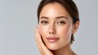 © buraratn - Woman with Natural Beauty and Radiant Skin Touching Face Against Soft Gray Background, Wellness and Skincare Concept Emphasized in Image