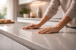 © MH - Close-up of a person's hands resting on a smooth, light grey kitchen countertop in a modern home.