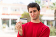 © luismolinero - Young handsome man holding a credit card at outdoors with sad expression