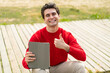 © luismolinero - Young handsome man holding a tablet at outdoors with thumbs up because something good has happened