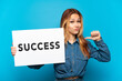 © luismolinero - Teenager girl over isolated blue background holding a placard with text SUCCESS with proud gesture