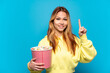 © luismolinero - Teenager girl holding popcorns over isolated blue background pointing up a great idea