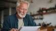 © CYBERPINK - Elderly man with a white beard and glasses sitting at a kitchen table. he is holding a tablet in his hands and appears to be engrossed in reading it.
