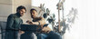© Prostock-studio - Two men are focused on a task in a well-lit room. They are using a laptop and a tablet while sitting next to a plant. They seem to discuss and share ideas actively.