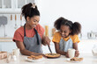 © Prostock-studio - Excited black mom and daughter in aprons tasting homemade berry pie, cutting cake and smiling, kitchen interior. Happy african american mother and kid teen girl baking together at home, copy space